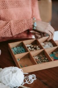 Hands crafting bracelets with colorful beads and a wooden organizer.